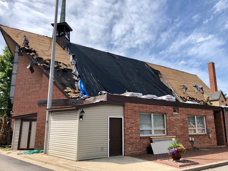 Street view of a steep Minneapolis church roof during shingle tear-off and roof deck installation